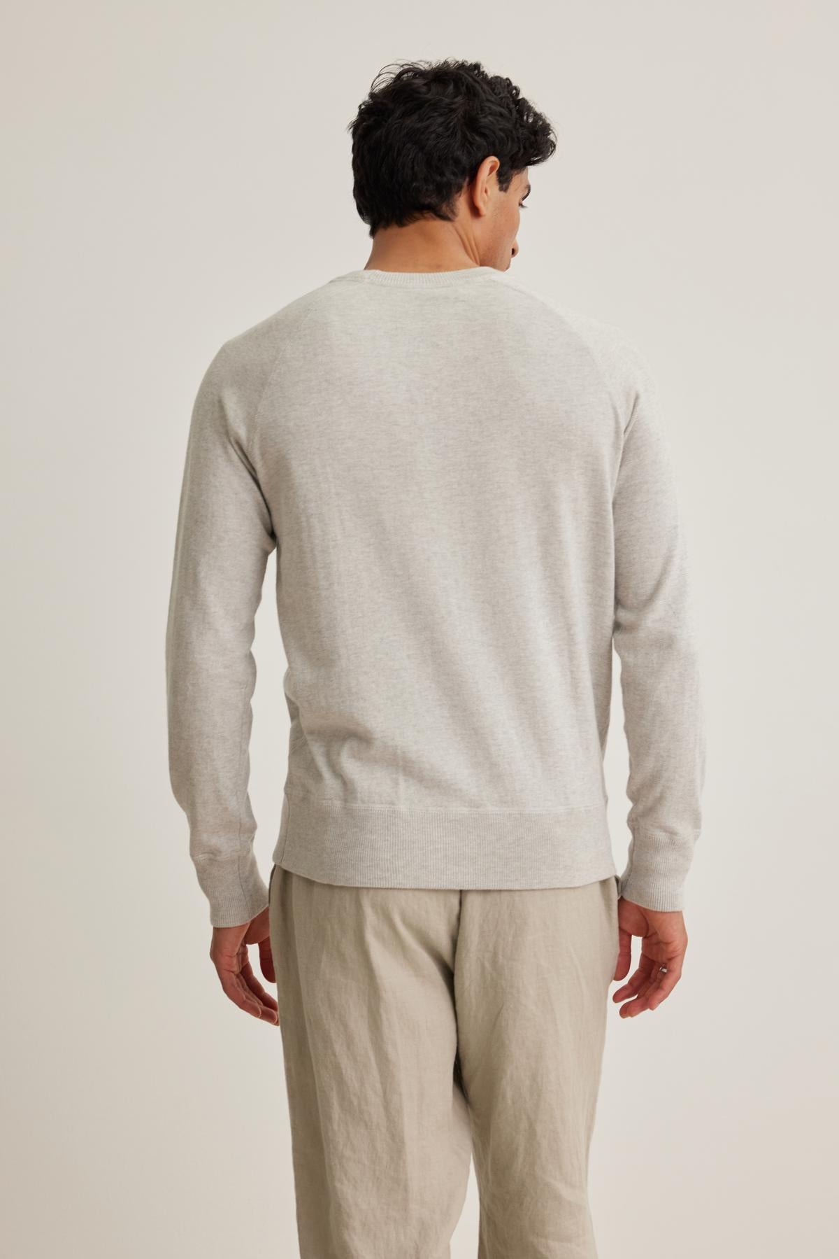   A man in a DARIO COTTON CASHMERE SWEATER by Velvet by Graham & Spencer, paired with beige pants, stands with his back to the camera against a plain background. 