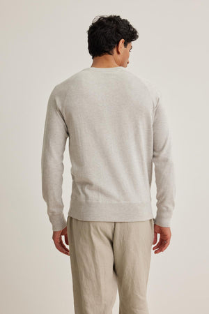 A man in a DARIO COTTON CASHMERE SWEATER by Velvet by Graham & Spencer, paired with beige pants, stands with his back to the camera against a plain background.