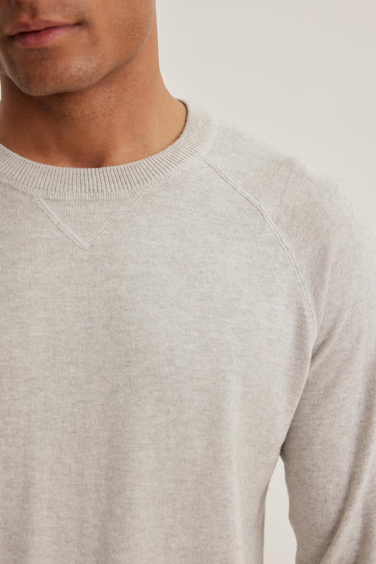   A person is wearing a Velvet by Graham & Spencer's DARIO COTTON CASHMERE SWEATER in light gray with a visible round neckline. Only the lower half of their face is shown against a plain, neutral background. 