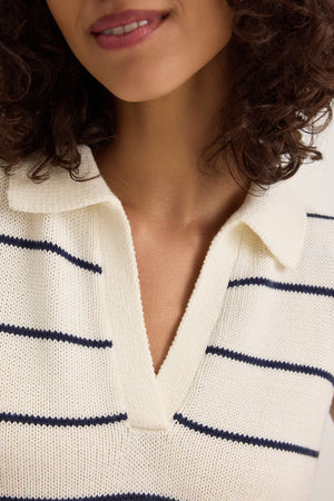 A person is styled in Velvet by Graham & Spencer's NAYLA sweater vest, layered over a white collared sweater with navy stripes. This classic piece, made from a soft cotton-cashmere blend, adds sophistication to any outfit.