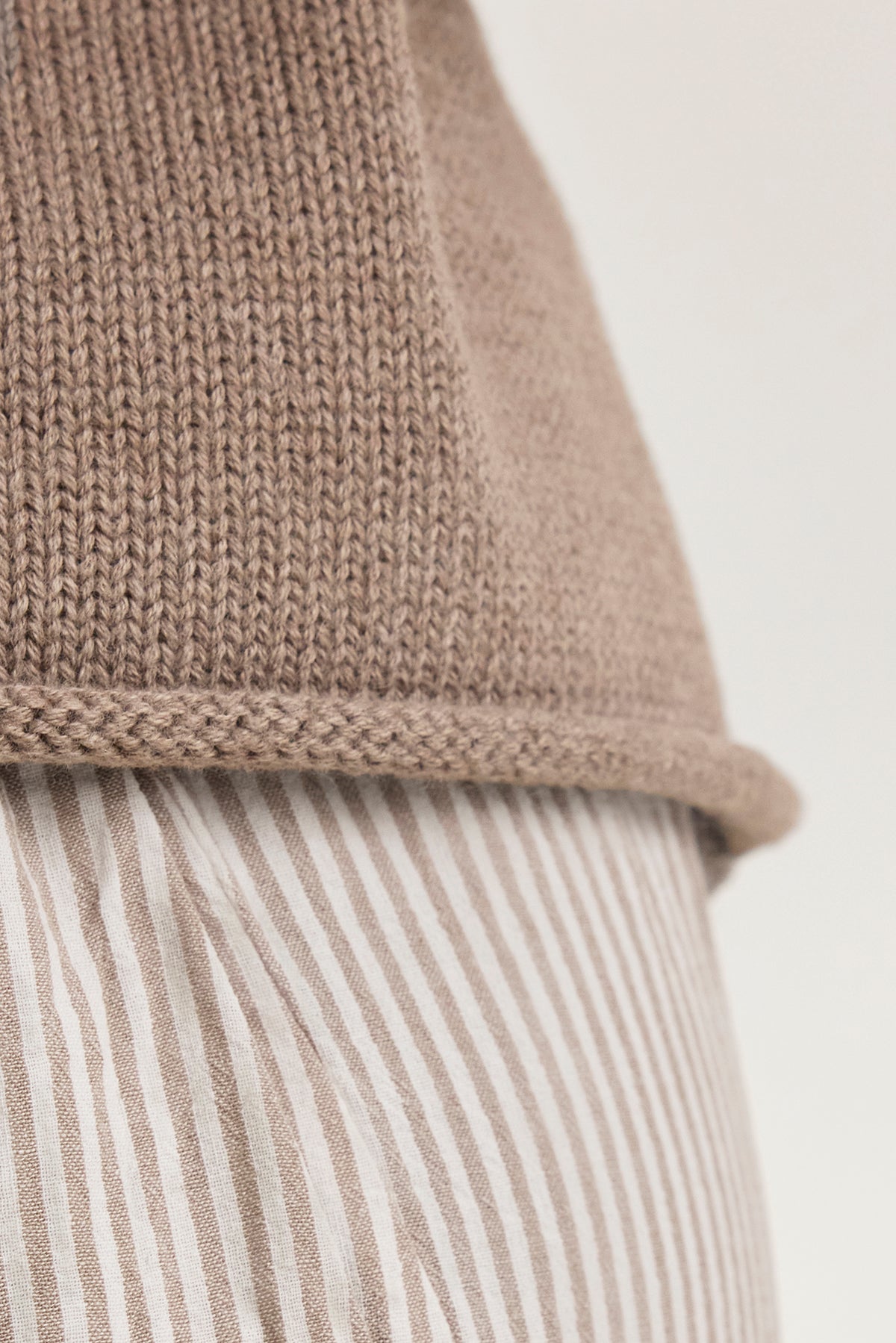   Close-up of the PAOLA COTTON CASHMERE SWEATER VEST by Velvet by Graham & Spencer, featuring a tan knit layered over a beige and white striped fabric, showcasing visible texture and pattern. 