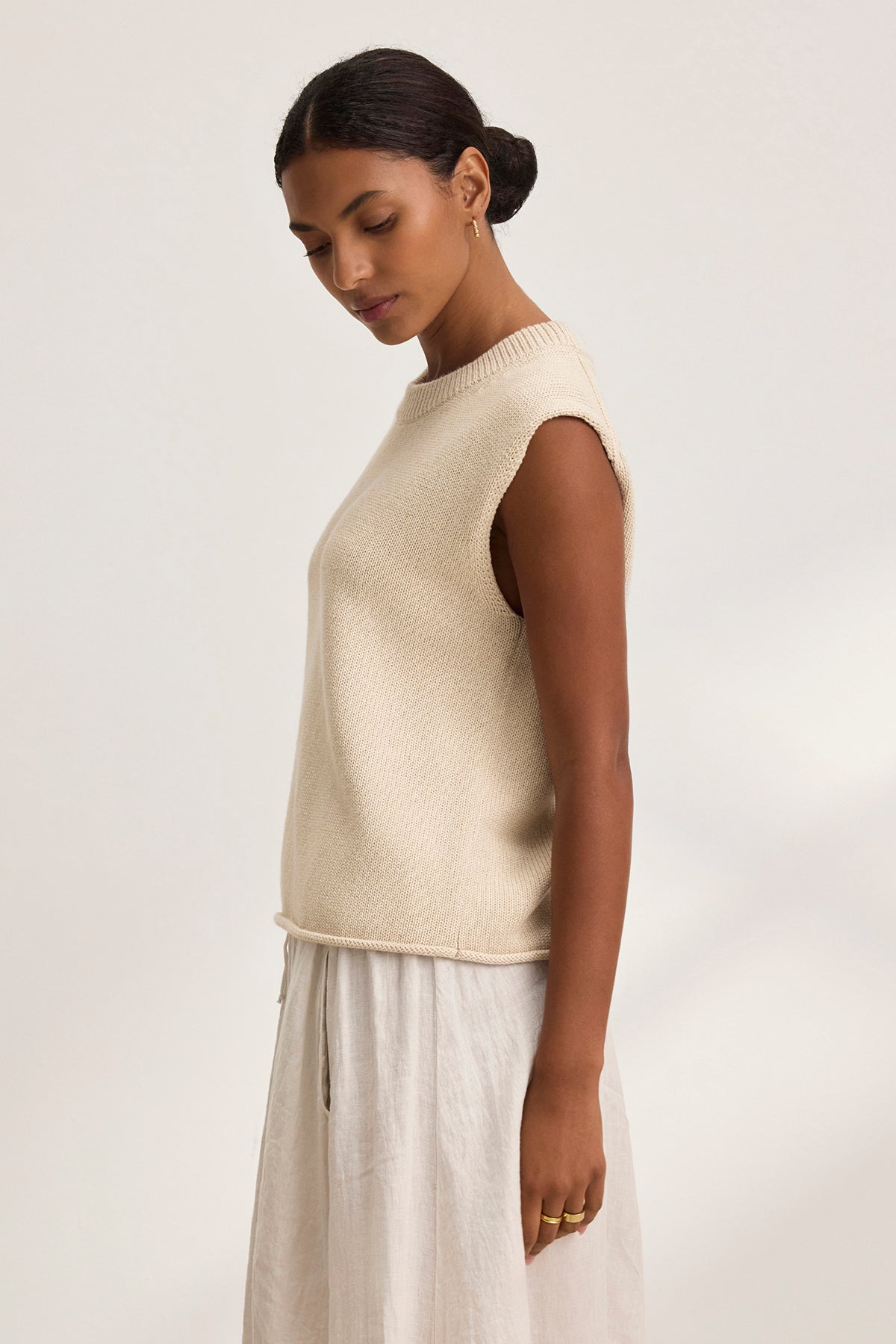   A woman in a PAOLA COTTON CASHMERE SWEATER VEST by Velvet by Graham & Spencer and a white skirt stands sideways against a plain background. 