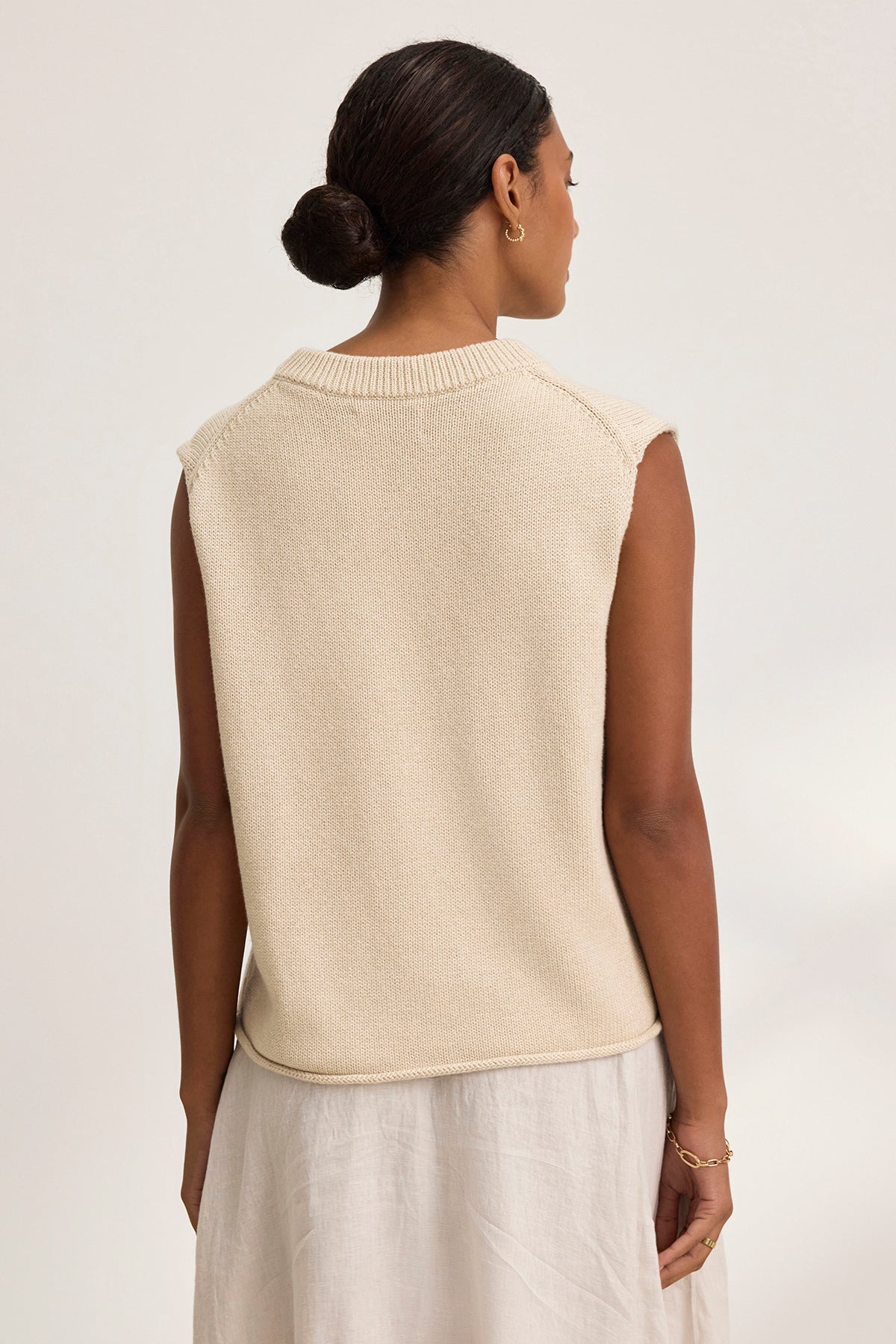   A person with hair in a bun wears the PAOLA Cotton Cashmere Sweater Vest from Velvet by Graham & Spencer and a white skirt, standing with their back to the camera. 