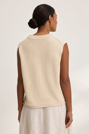 A person with hair in a bun wears the PAOLA Cotton Cashmere Sweater Vest from Velvet by Graham & Spencer and a white skirt, standing with their back to the camera.