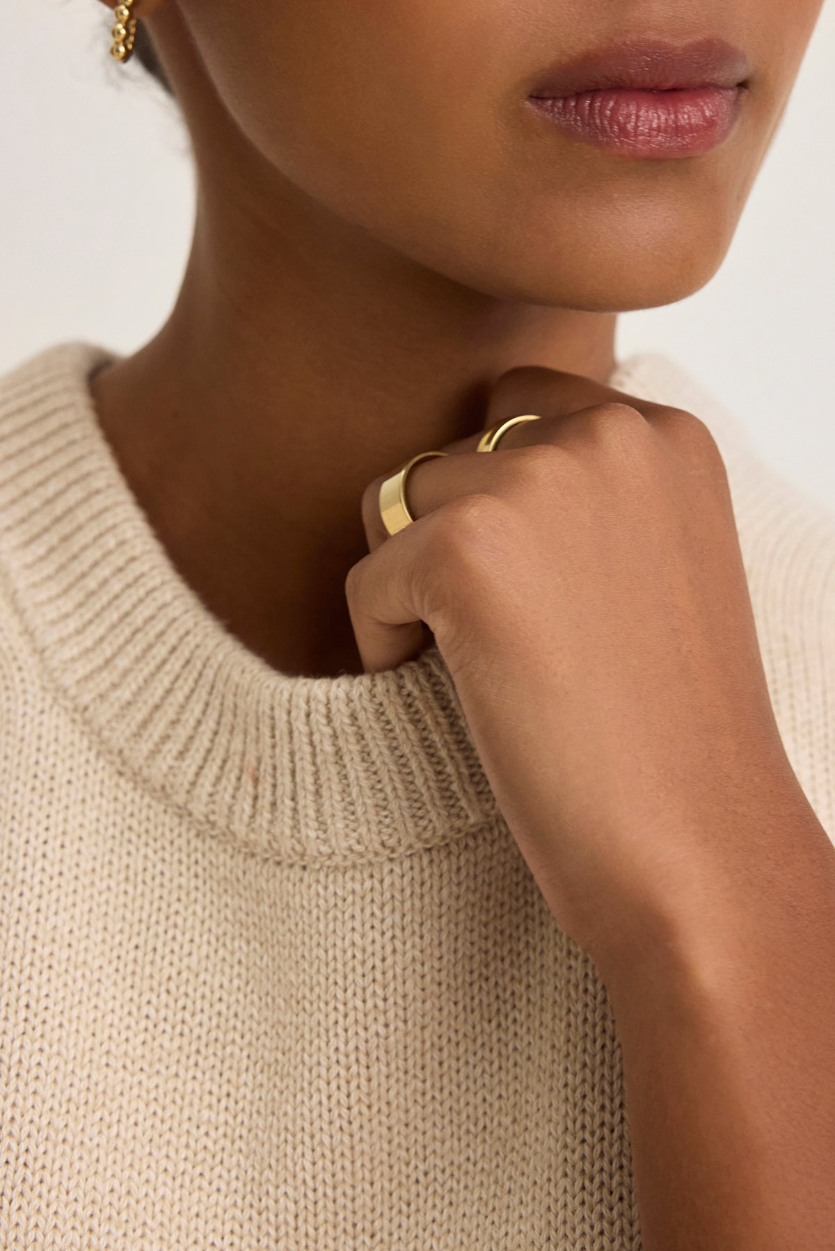   Close-up of a person wearing a PAOLA COTTON CASHMERE SWEATER VEST by Velvet by Graham & Spencer, with a gold ring, an earring, and their hand partially covering their mouth. 