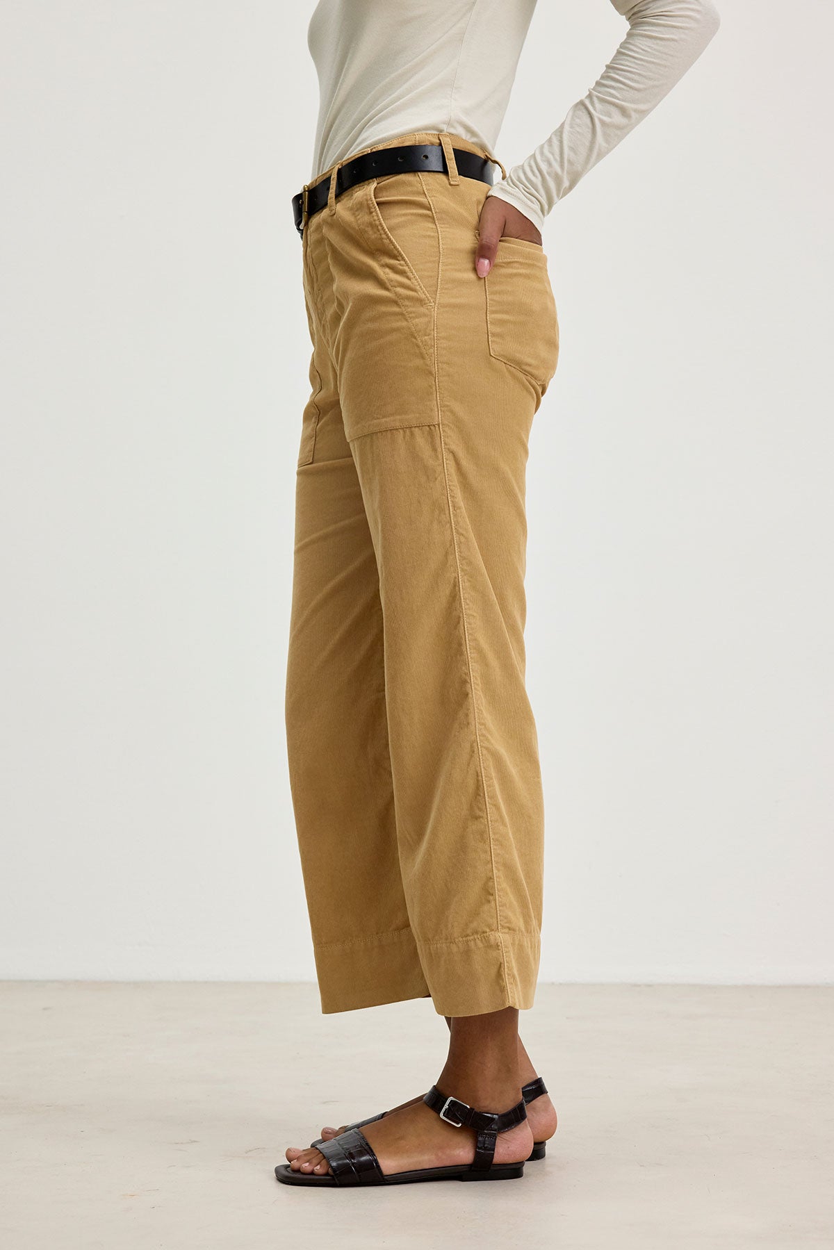 A person standing in VERA CORDUROY PANTS by Velvet by Graham & Spencer, a white long-sleeve top, and black sandals on a plain background.-37745668784321