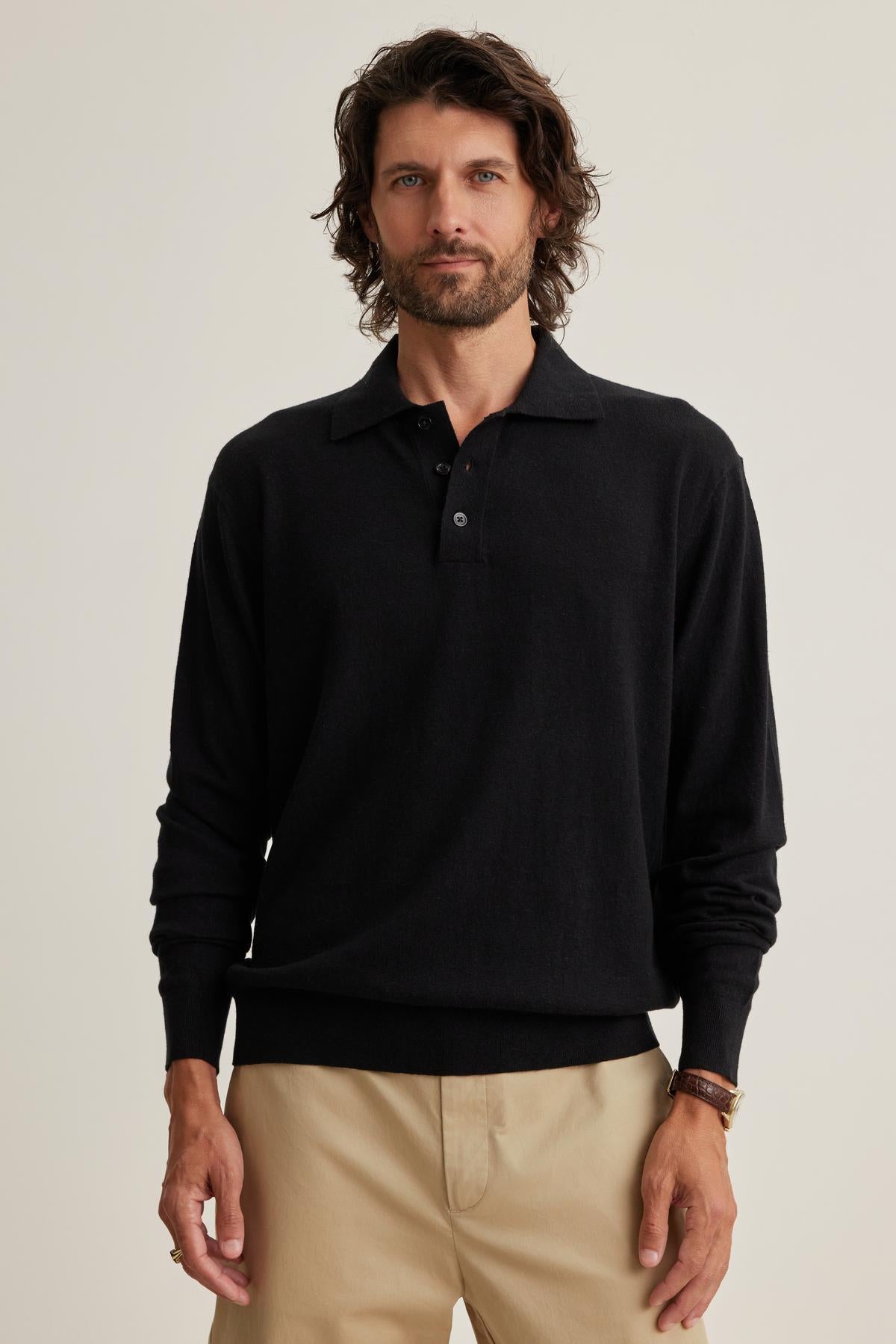 A man with wavy hair is wearing a black Velvet by Graham & Spencer MATTEO Cotton Linen Sweater Polo and beige pants while standing against a plain background.-38643324813505