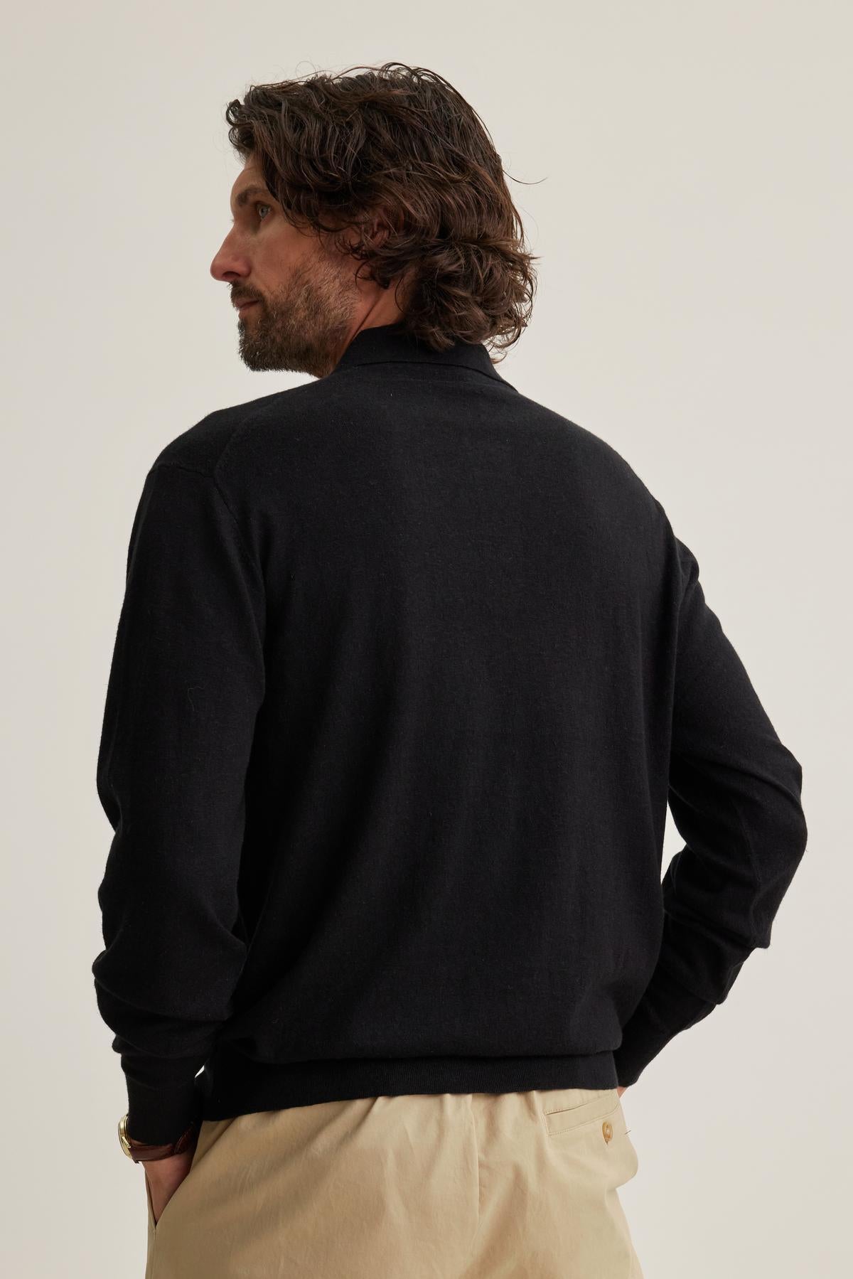   A man with wavy hair is wearing a Velvet by Graham & Spencer MATTEO Cotton Linen Sweater Polo and beige pants, facing away against a plain background. 