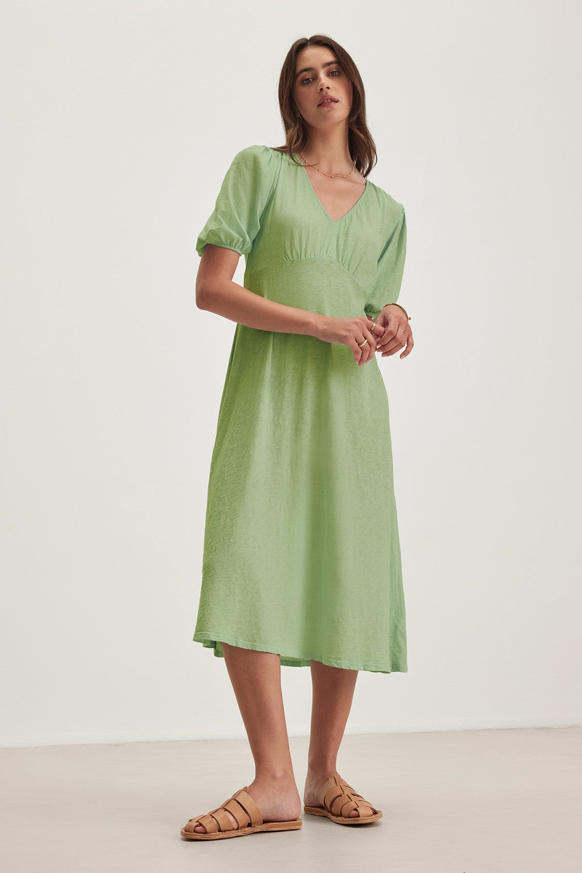 Barefoot in her light green PARKER DRESS by Velvet by Graham & Spencer, a woman stands against a plain white background and light-colored floor. The figure-skimming cotton slub dress enhances her effortless style.-38663138083009