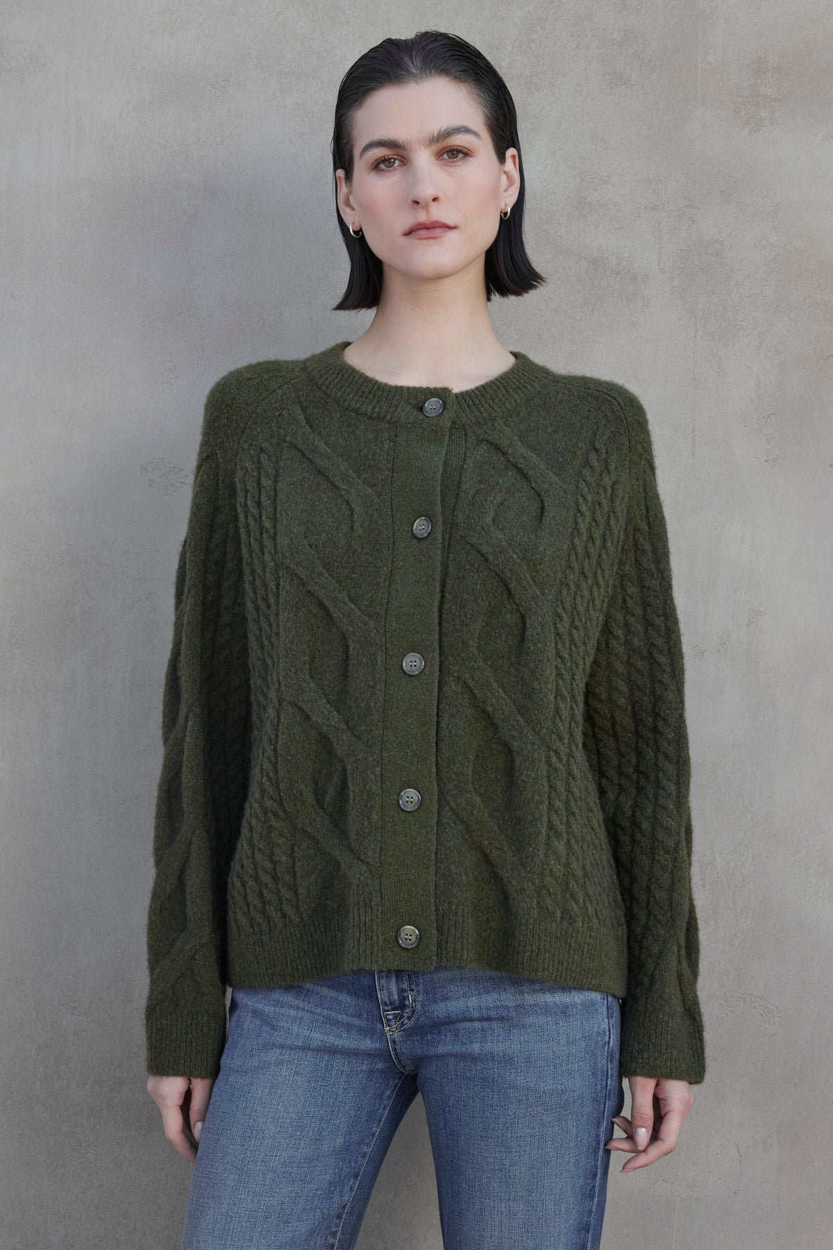   Person wearing a BEACHWOOD CARDIGAN by Velvet by Jenny Graham, paired with blue jeans, standing against a gray textured background. 