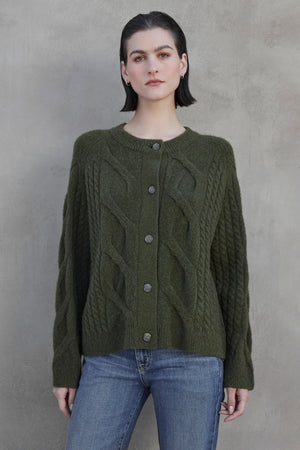 Person wearing a BEACHWOOD CARDIGAN by Velvet by Jenny Graham, paired with blue jeans, standing against a gray textured background.