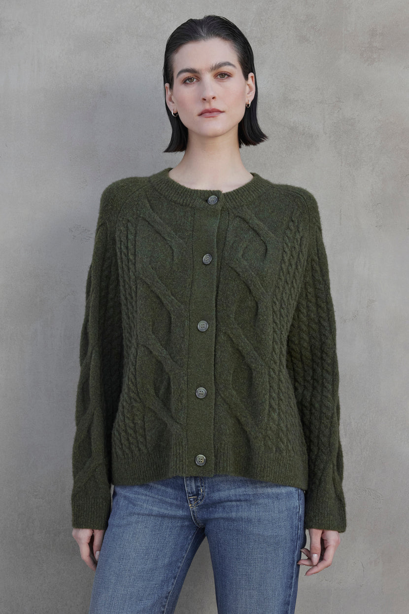 Person wearing a BEACHWOOD CARDIGAN by Velvet by Jenny Graham, paired with blue jeans, standing against a gray textured background.