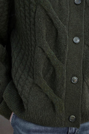 Close-up of the BEACHWOOD CARDIGAN, a dark green cable knit piece by Velvet by Jenny Graham, featuring black buttons and paired with blue jeans.