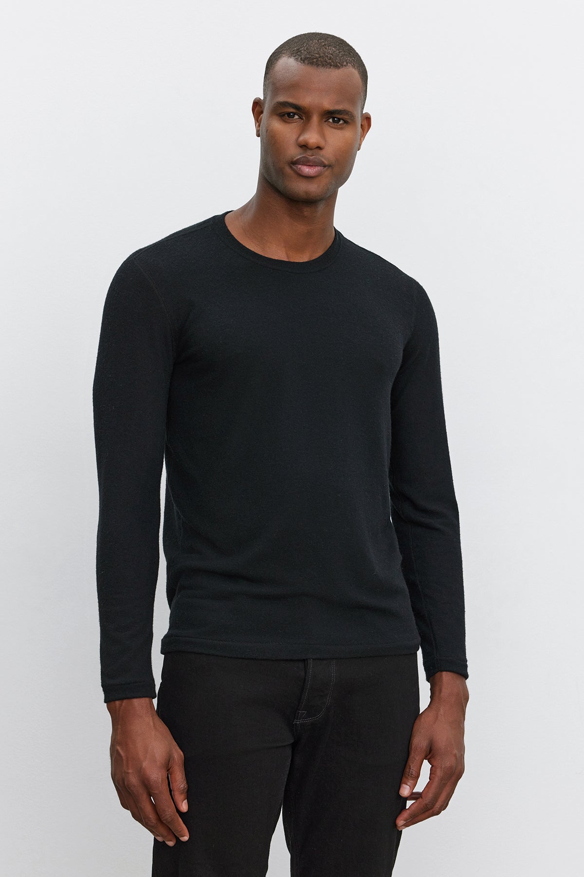   A man wearing a Velvet by Graham & Spencer BECKER CREW black fitted crew neck long-sleeve shirt and black pants stands against a plain white background, looking at the camera. The ultra-soft jersey fabric makes it perfect for daily wear. 