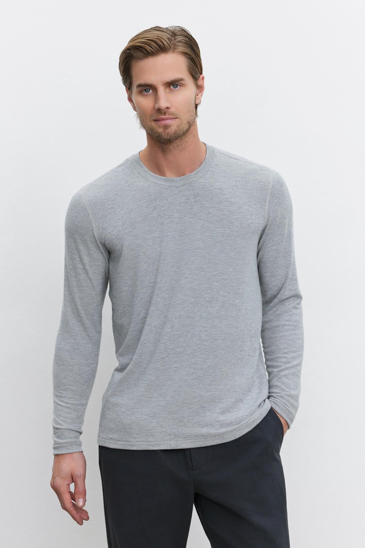   A person wearing a light gray BECKER CREW jersey long-sleeve shirt by Velvet by Graham & Spencer and dark pants stands against a plain white background. 