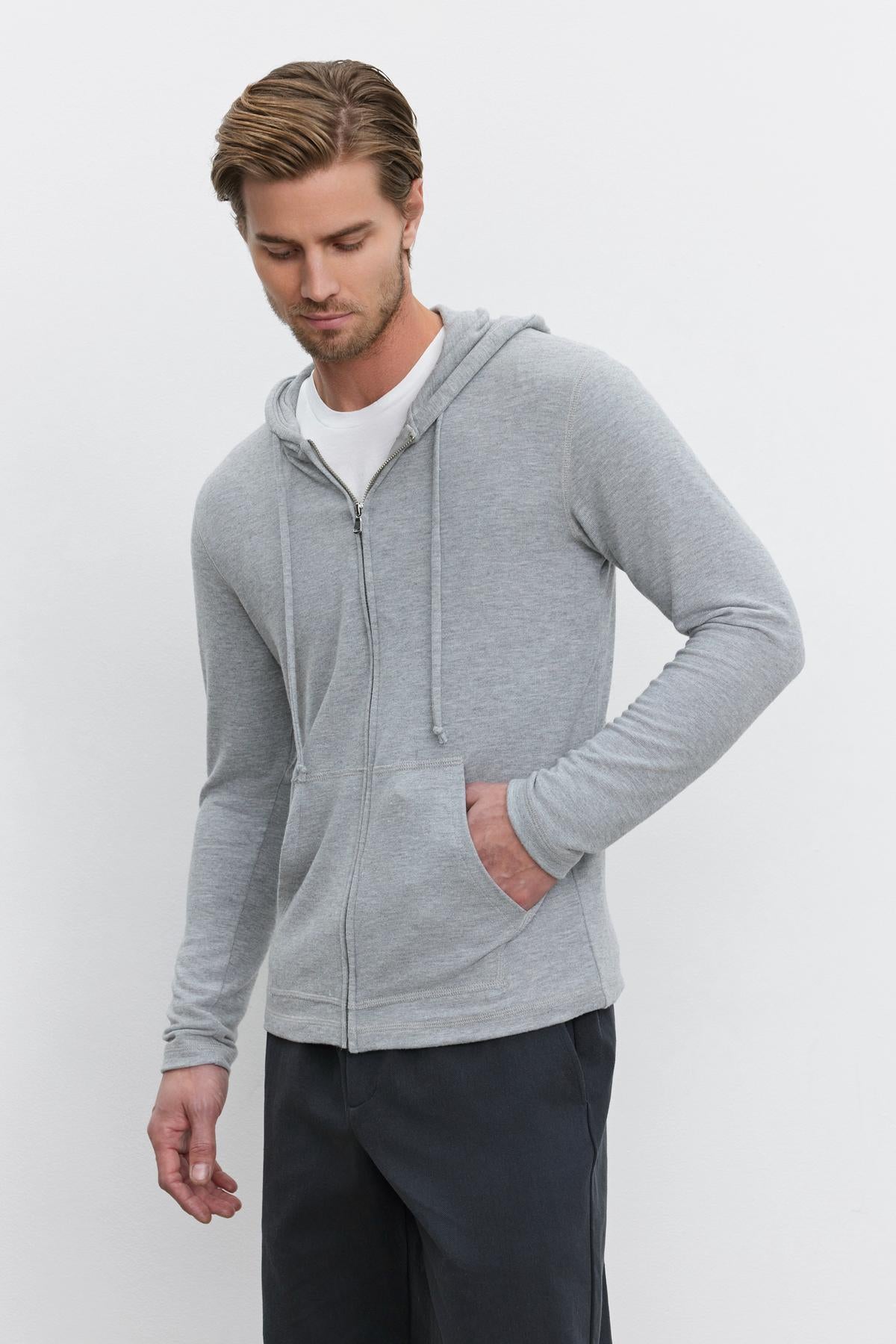   A person in a LOUDON HOODIE by Velvet by Graham & Spencer and dark pants stands against a plain background, with one hand in the pocket and the other resting beside the body. 