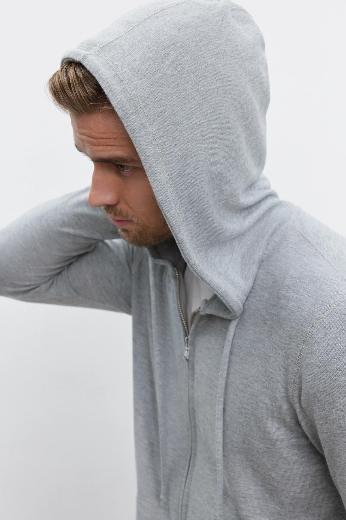   A person wearing the LOUDON HOODIE from Velvet by Graham & Spencer with the hood up, looking to the side, and touching the back of their head. 