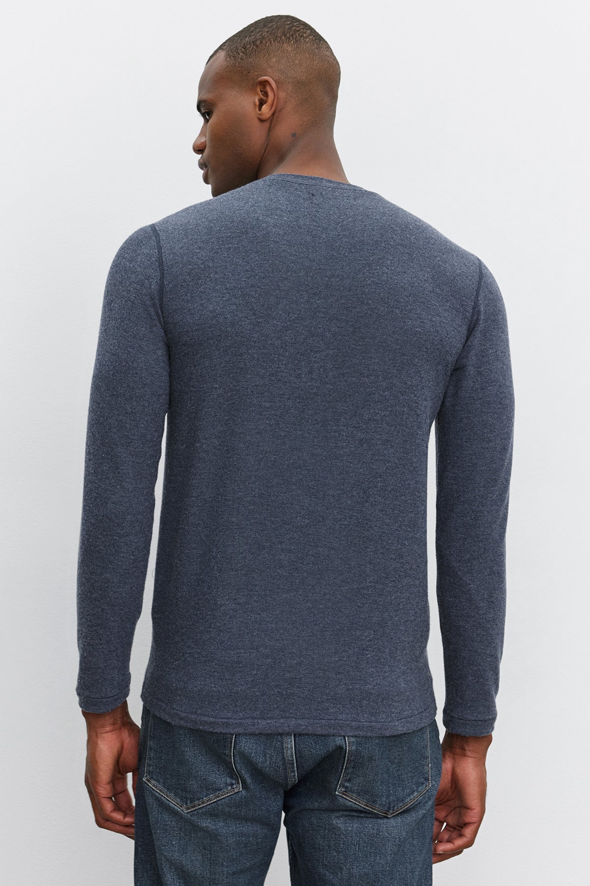   A person with short hair wearing a long-sleeved, dark gray RYLAND HENLEY from Velvet by Graham & Spencer and jeans stands with their back to the camera. 