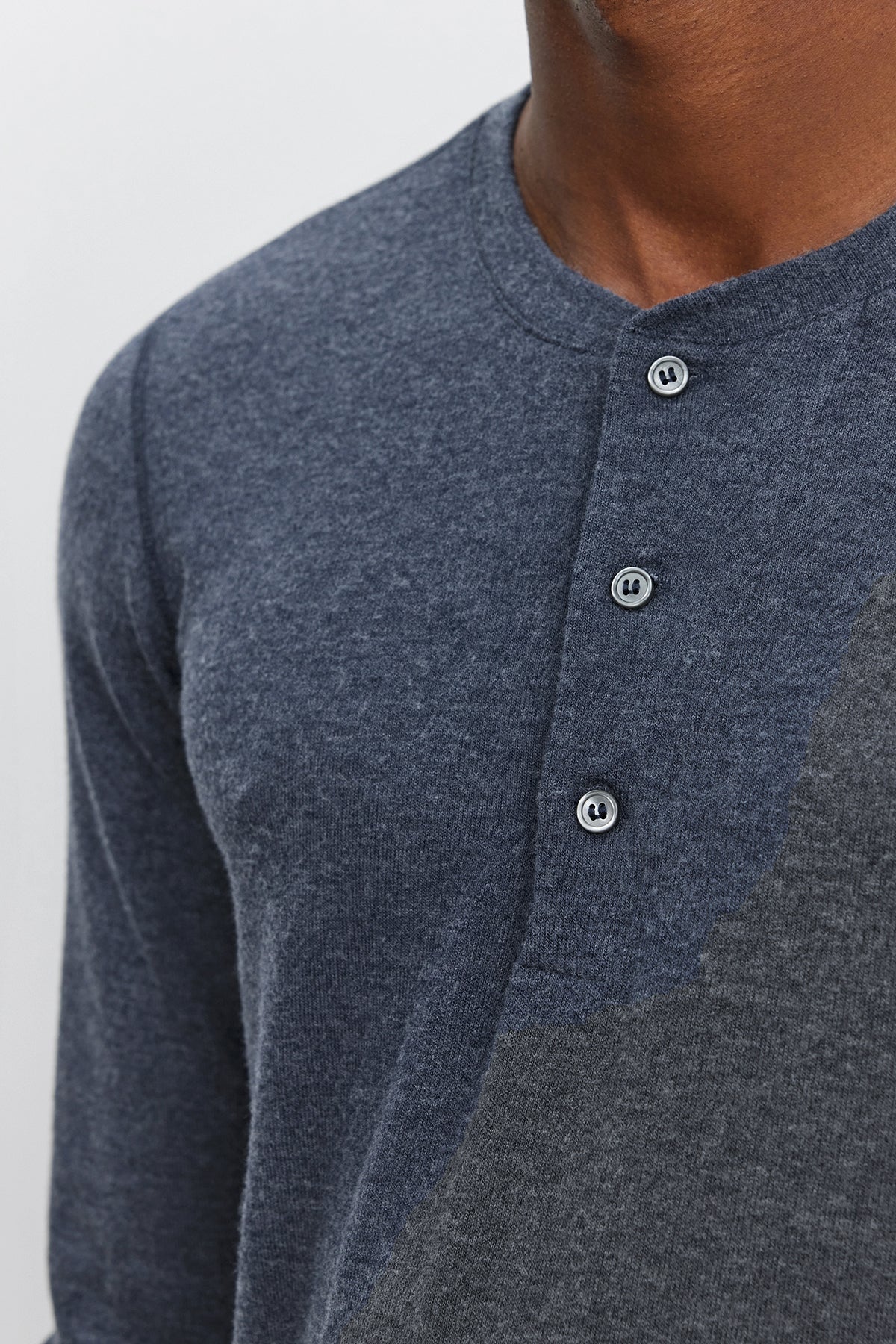   Close-up of a person wearing the Velvet by Graham & Spencer RYLAND HENLEY, a dark blue 3-button henley with contrasting fabric on one side. Made from cozy jersey, this versatile piece combines comfort and style effortlessly. The person's face is not visible. 