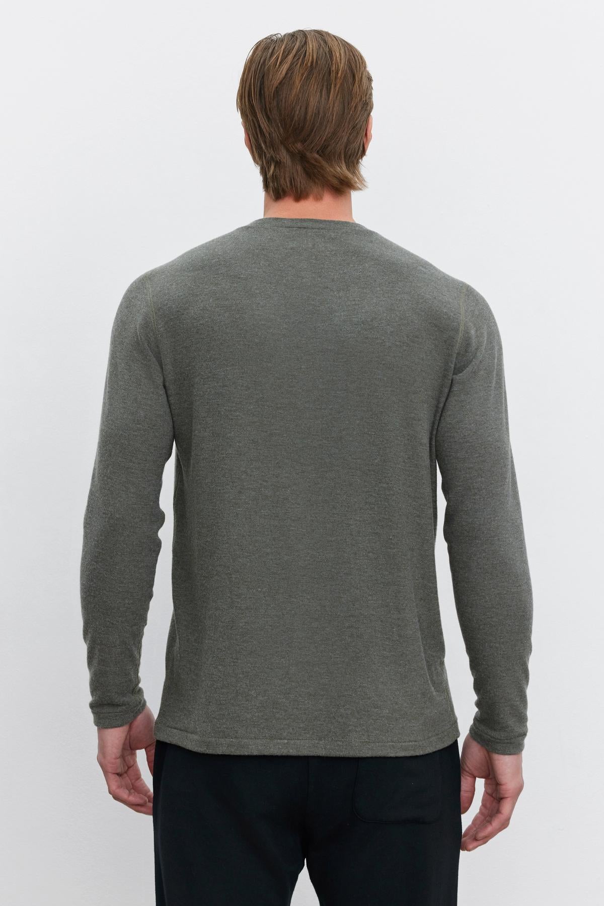   A person with short brown hair is standing with their back to the camera, wearing the versatile Velvet by Graham & Spencer RYLAND HENLEY in gray and black pants—this piece perfectly complements the outfit. 