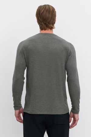 A person with short brown hair is standing with their back to the camera, wearing the versatile Velvet by Graham & Spencer RYLAND HENLEY in gray and black pants—this piece perfectly complements the outfit.