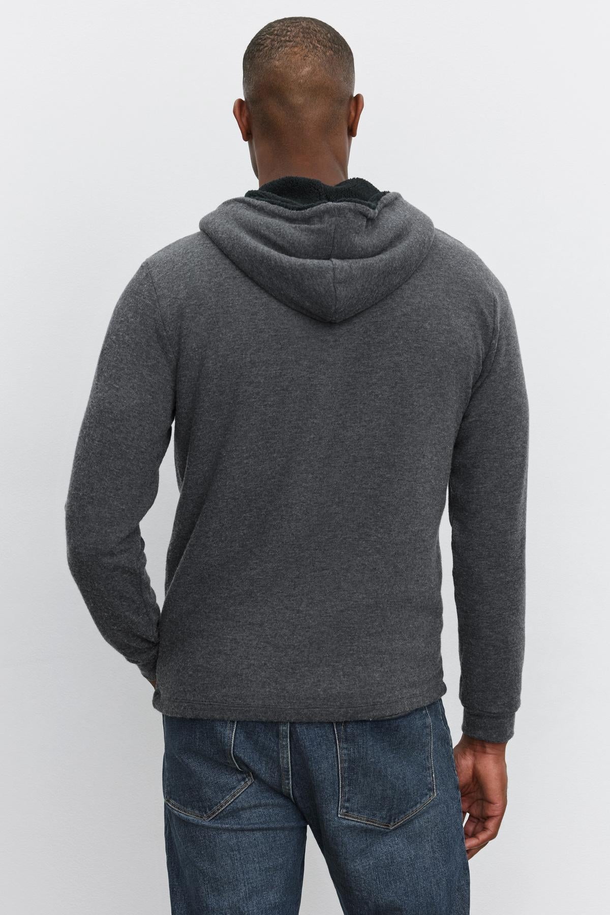   A person wearing the Velvet by Graham & Spencer SALVADORE HOODIE in dark gray, paired with blue jeans, is seen from the back, standing against a plain light background. 