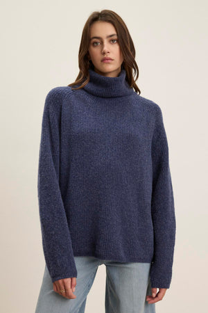 A person is wearing the JUDITH TURTLENECK SWEATER from Velvet by Graham & Spencer, styled with light blue jeans, standing against a plain background.