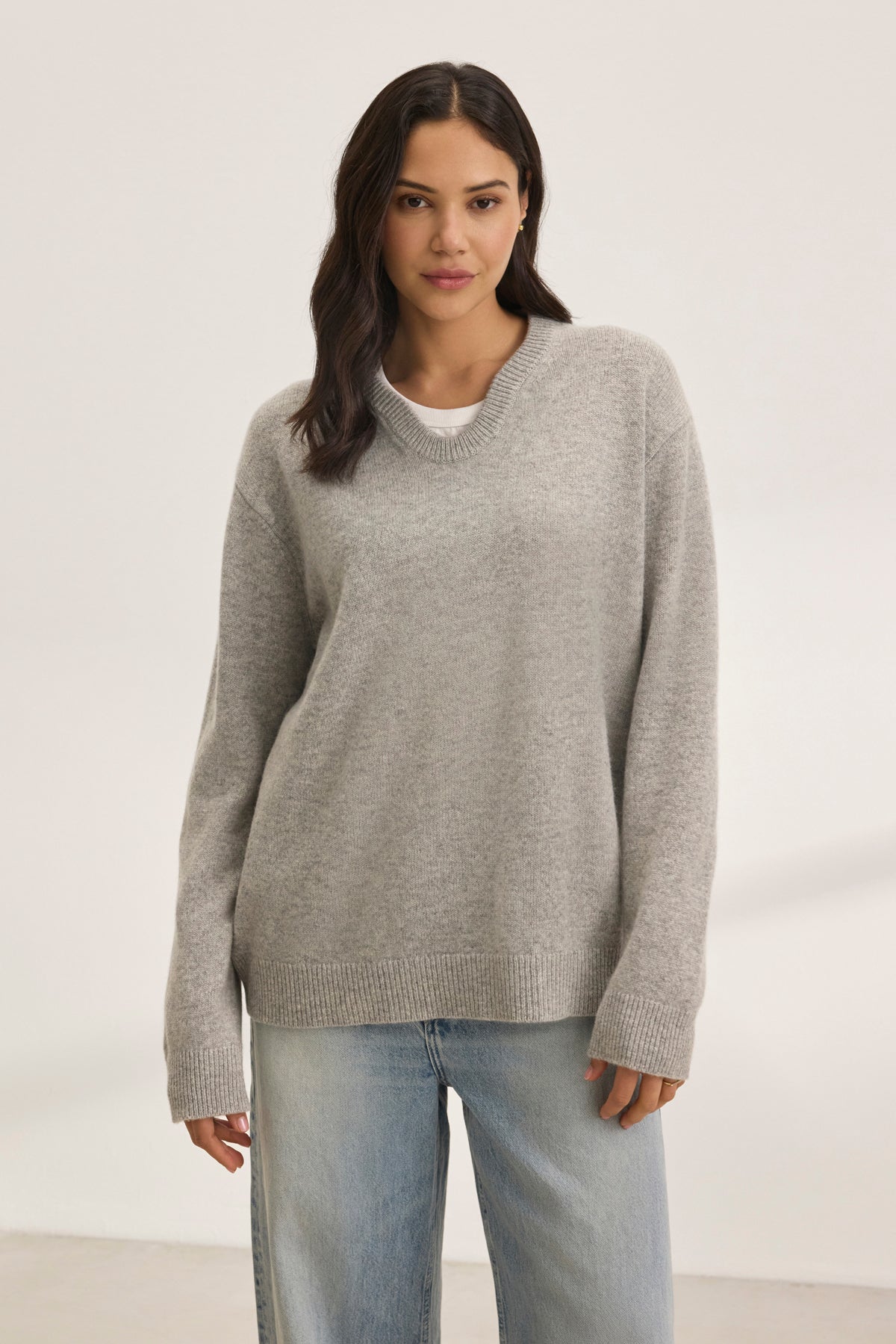   A person is wearing a Velvet by Graham & Spencer STEVIE WOOL CASHMERE SWEATER in oversized gray, paired with light blue jeans against a plain background. 