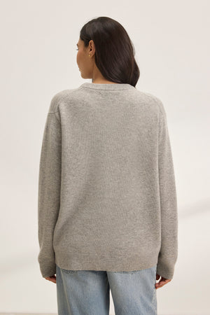 Someone is clad in a cozy, oversized gray STEVIE WOOL CASHMERE SWEATER by Velvet by Graham & Spencer. They pair it with blue jeans and stand facing away against a plain background.