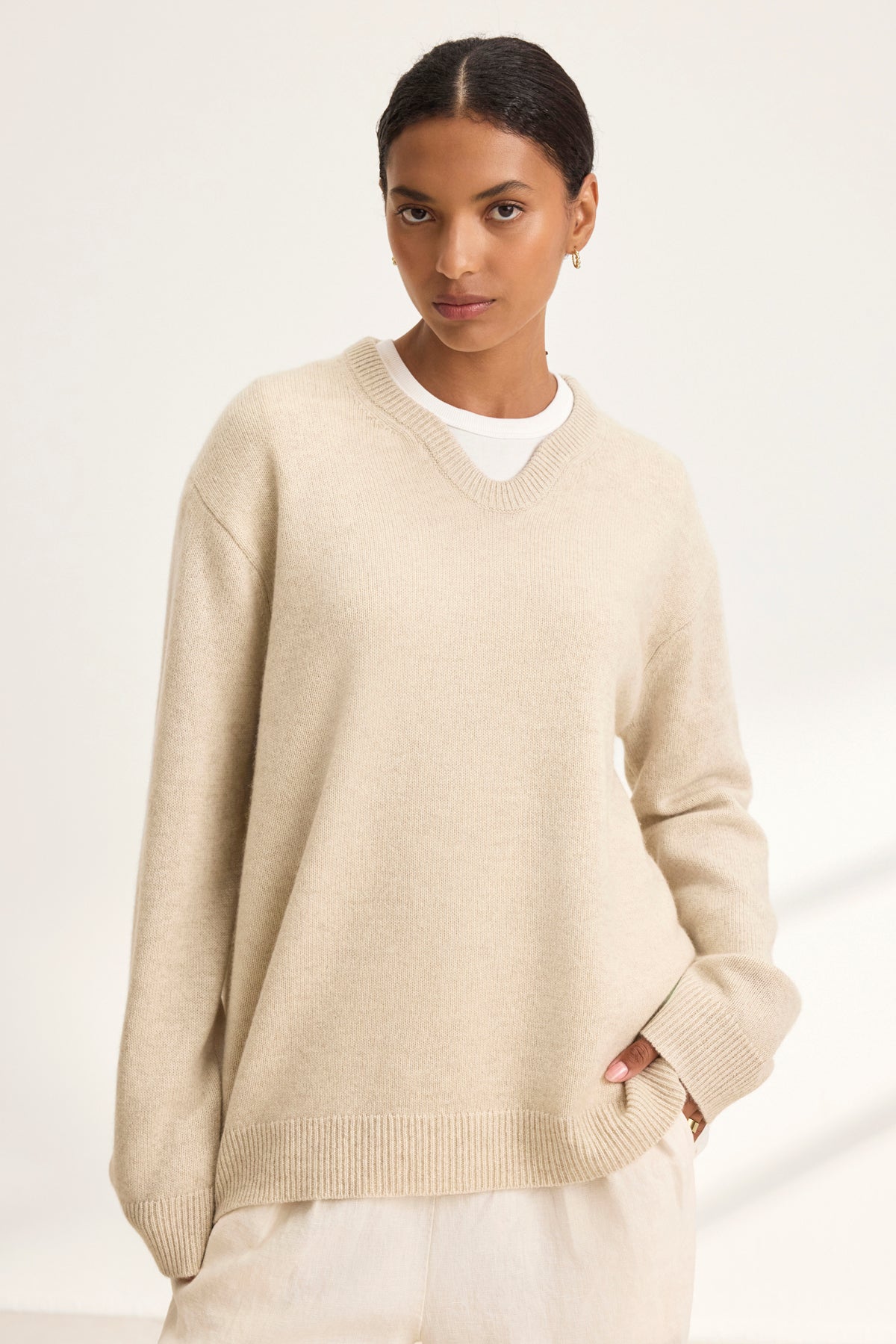   Against a plain backdrop, a person wears the oversized STEVIE WOOL CASHMERE SWEATER by Velvet by Graham & Spencer in beige, layered over a crisp white shirt, embodying cozy dressing with its luxurious wool-cashmere blend. 