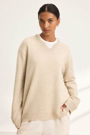 Against a plain backdrop, a person wears the oversized STEVIE WOOL CASHMERE SWEATER by Velvet by Graham & Spencer in beige, layered over a crisp white shirt, embodying cozy dressing with its luxurious wool-cashmere blend.