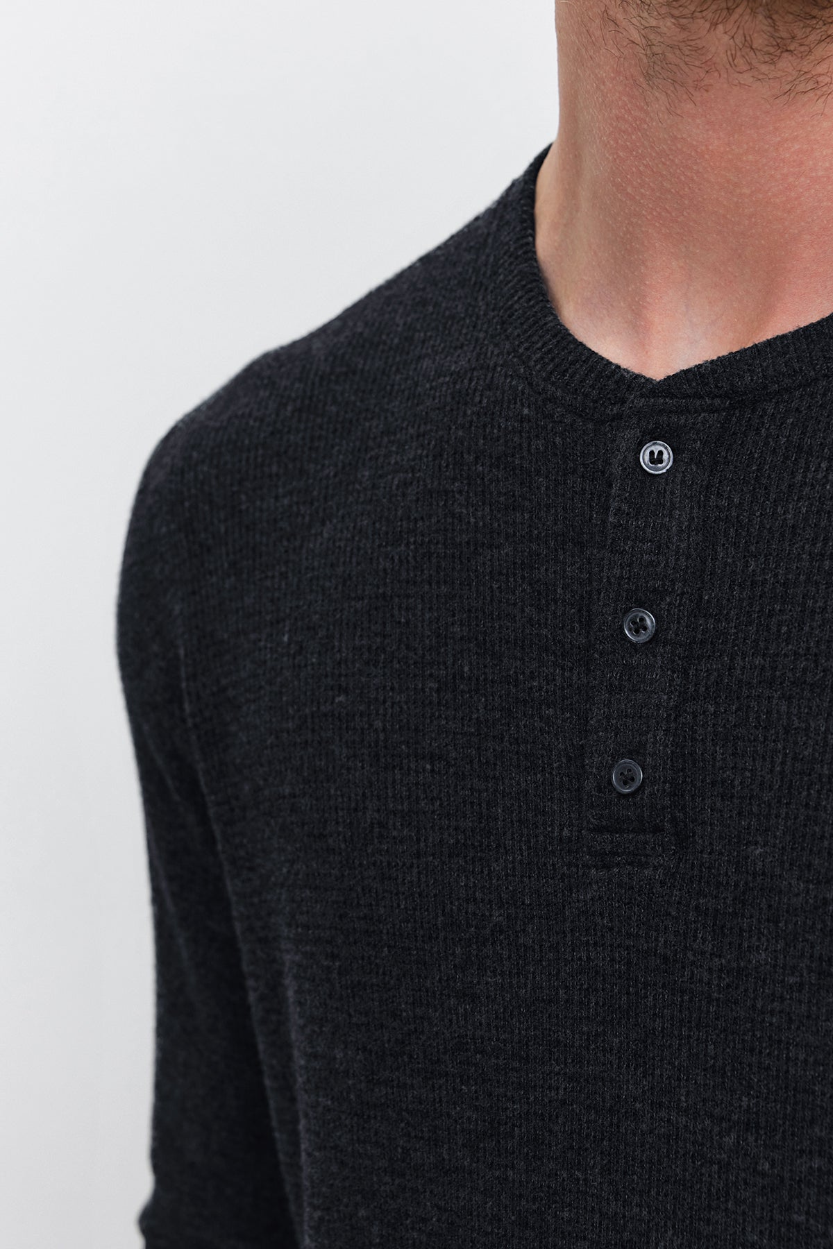 Close-up of a person's torso wearing the AMBROSE HENLEY, made of dark ribbed triblend cozy thermal fabric, featuring a three-button placket by Velvet by Graham & Spencer. The background is plain white.-37893849186497