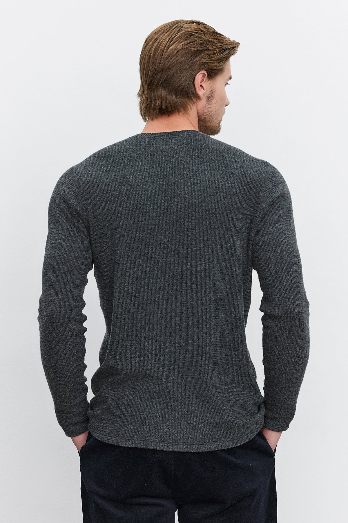   A person with light brown hair stands facing away, wearing the AMBROSE HENLEY by Velvet by Graham & Spencer, which features a three-button placket, along with black pants. 