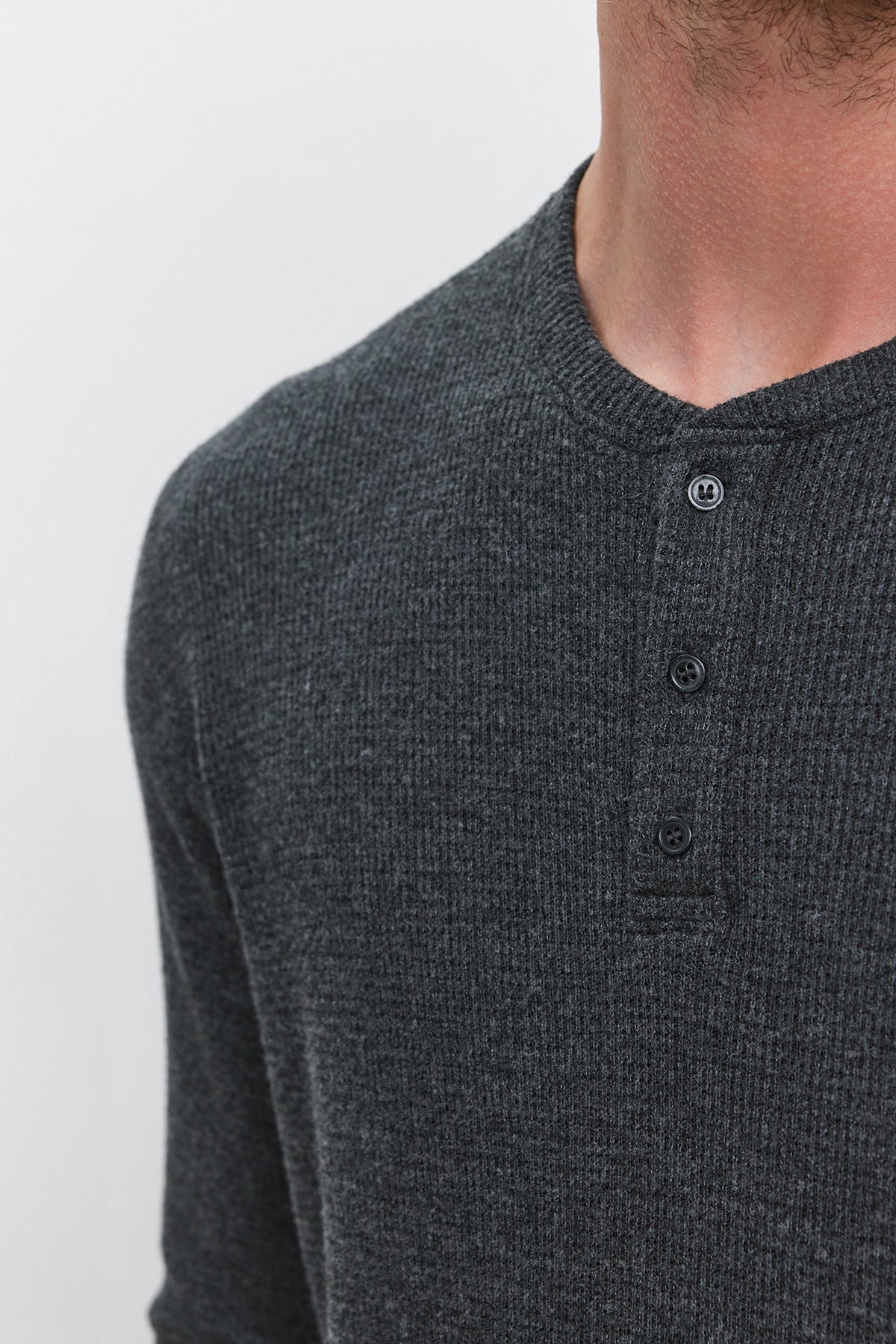   Close-up view of a person wearing Velvet by Graham & Spencer's AMBROSE HENLEY in dark gray triblend cozy thermal fabric with a three-button placket; only the neck and upper chest are visible against a plain background. 