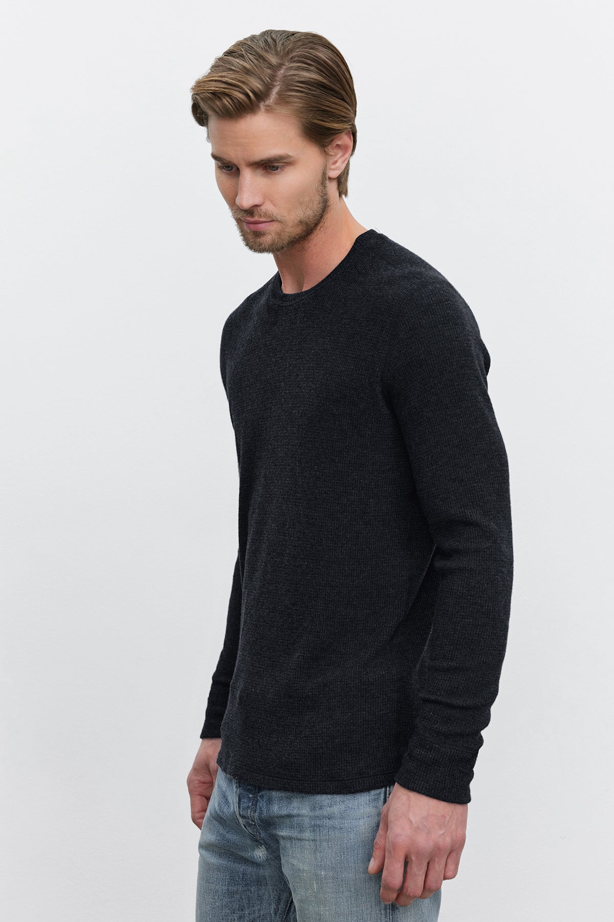 A man with light hair, wearing a versatile TOBIAS CREW dark long-sleeved shirt made of thermal fabric by Velvet by Graham & Spencer and blue jeans, stands against a plain white background.-37893931499713