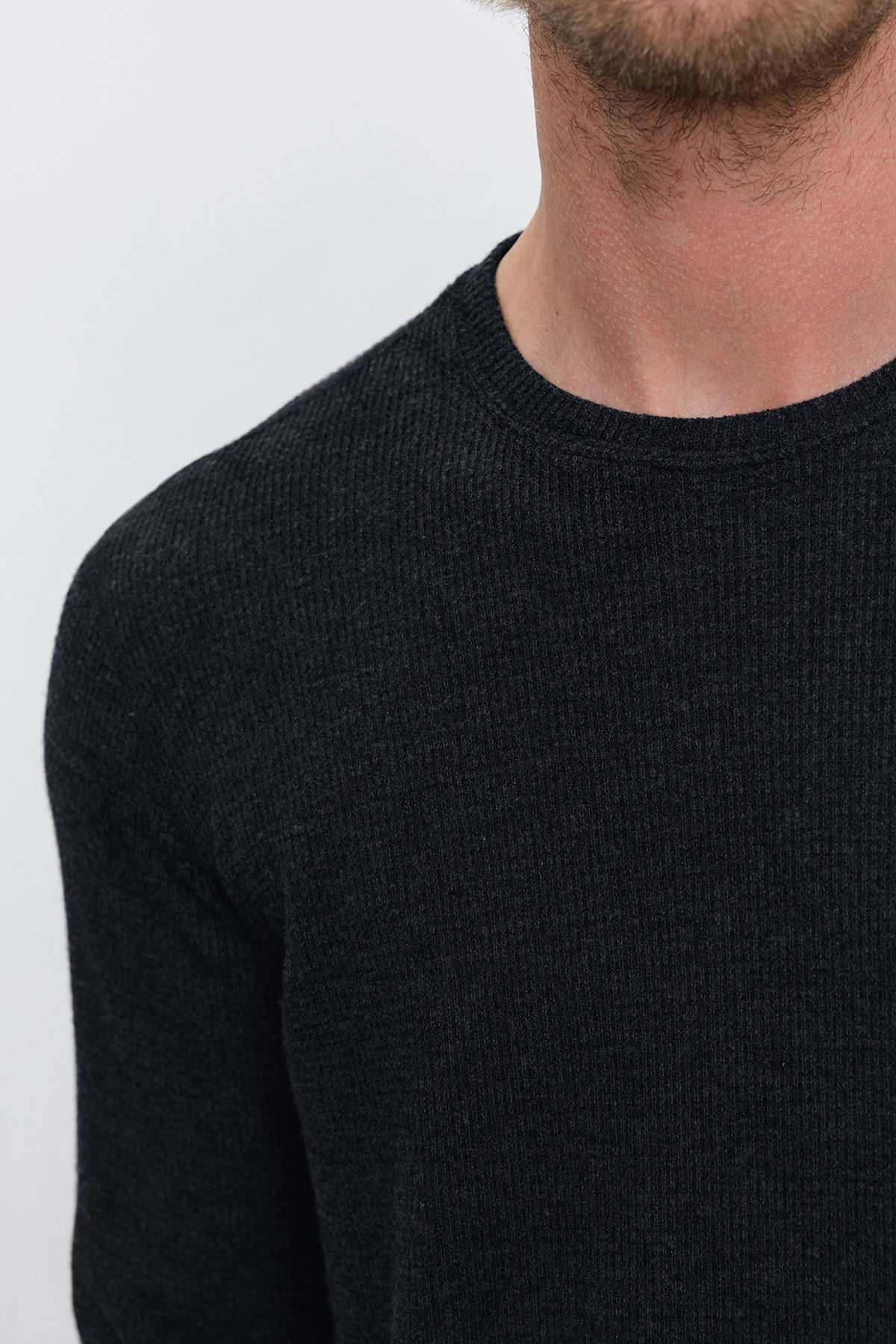   Close-up of a person wearing the TOBIAS CREW, a dark gray, long-sleeve sweater crafted from versatile thermal fabric by Velvet by Graham & Spencer, against a plain background. The photo captures the upper torso and crew neckline, highlighting the texture and warmth of the knit. 