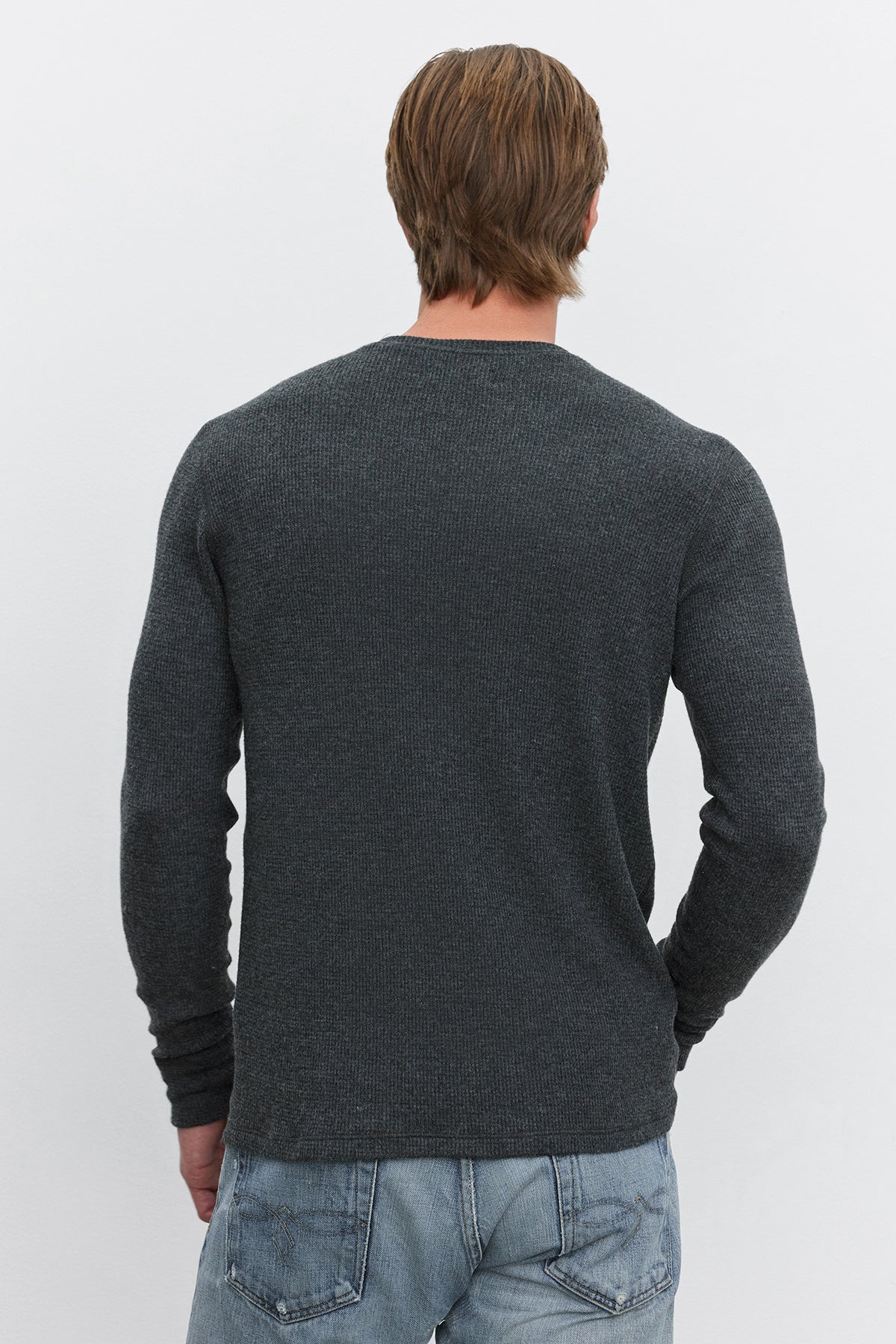   A person with short brown hair is shown from the back, wearing a long-sleeved TOBIAS CREW in dark grey textured fabric made of triblend cozy thermal material by Velvet by Graham & Spencer, paired with light blue jeans. 