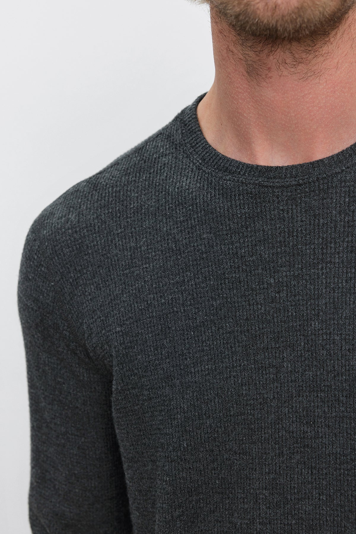   Close-up of a person wearing the TOBIAS CREW by Velvet by Graham & Spencer, a dark gray ribbed knit sweater, with the focus on the chest and a partial view of the neck and chin. The classic neckline enhances both comfort and versatility. 