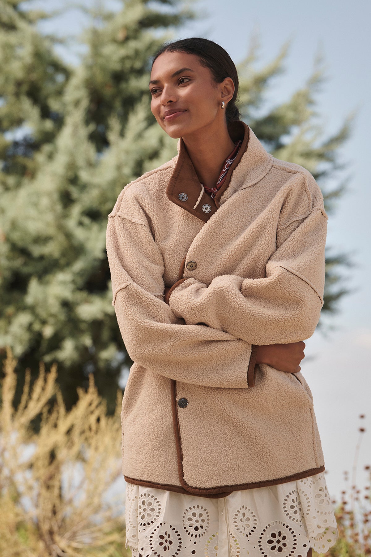 A person outdoors, surrounded by trees, is dressed in the ALBANY LUXE SHERPA REVERSIBLE JACKET from Velvet by Graham & Spencer, showcasing its eco-friendly faux sherpa lining.-38218871668929