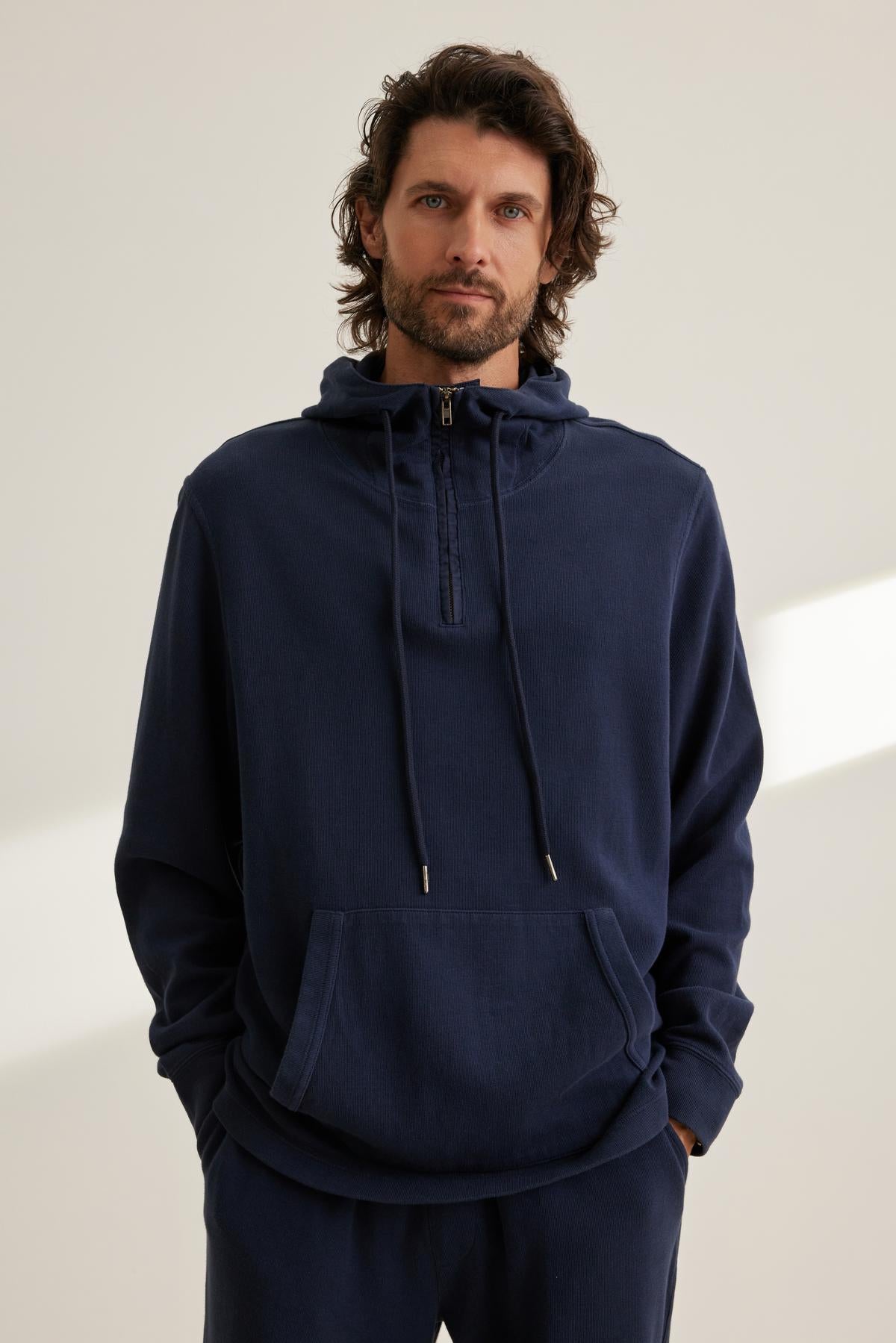 A person wearing the MORTY HOODIE, a dark blue half-zip hoodie with a front pocket from Velvet by Graham & Spencer, stands against a plain background.-38643326550209