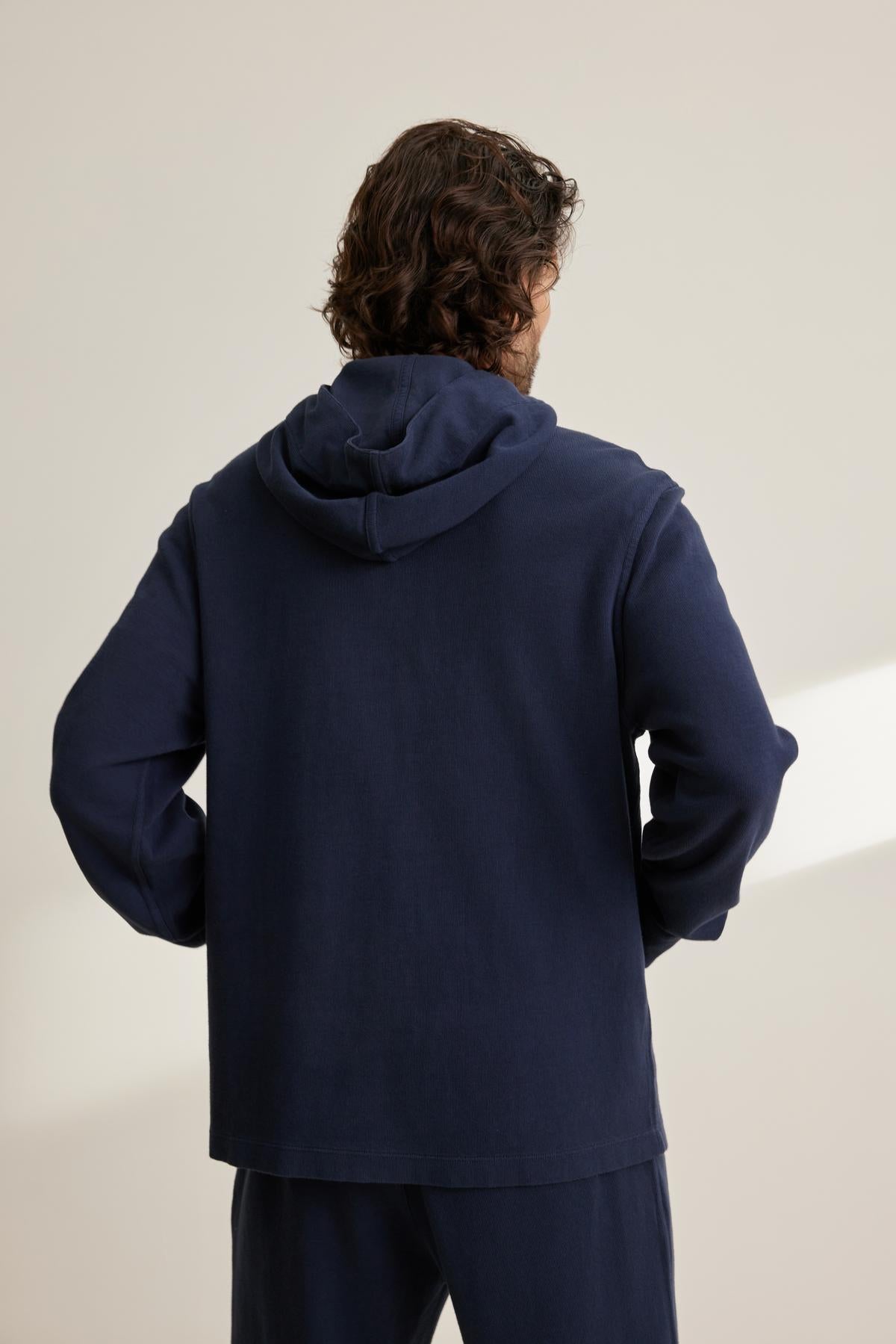   A person with curly hair facing away wears a navy blue MORTY HOODIE by Velvet by Graham & Spencer and matching pants against a neutral background. 