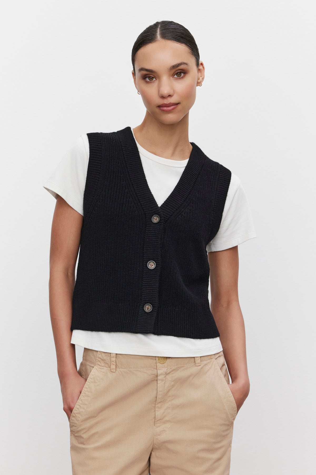   A person wearing the LU SWEATER VEST by Velvet by Graham & Spencer over a white T-shirt and beige trousers, standing against a plain background. 