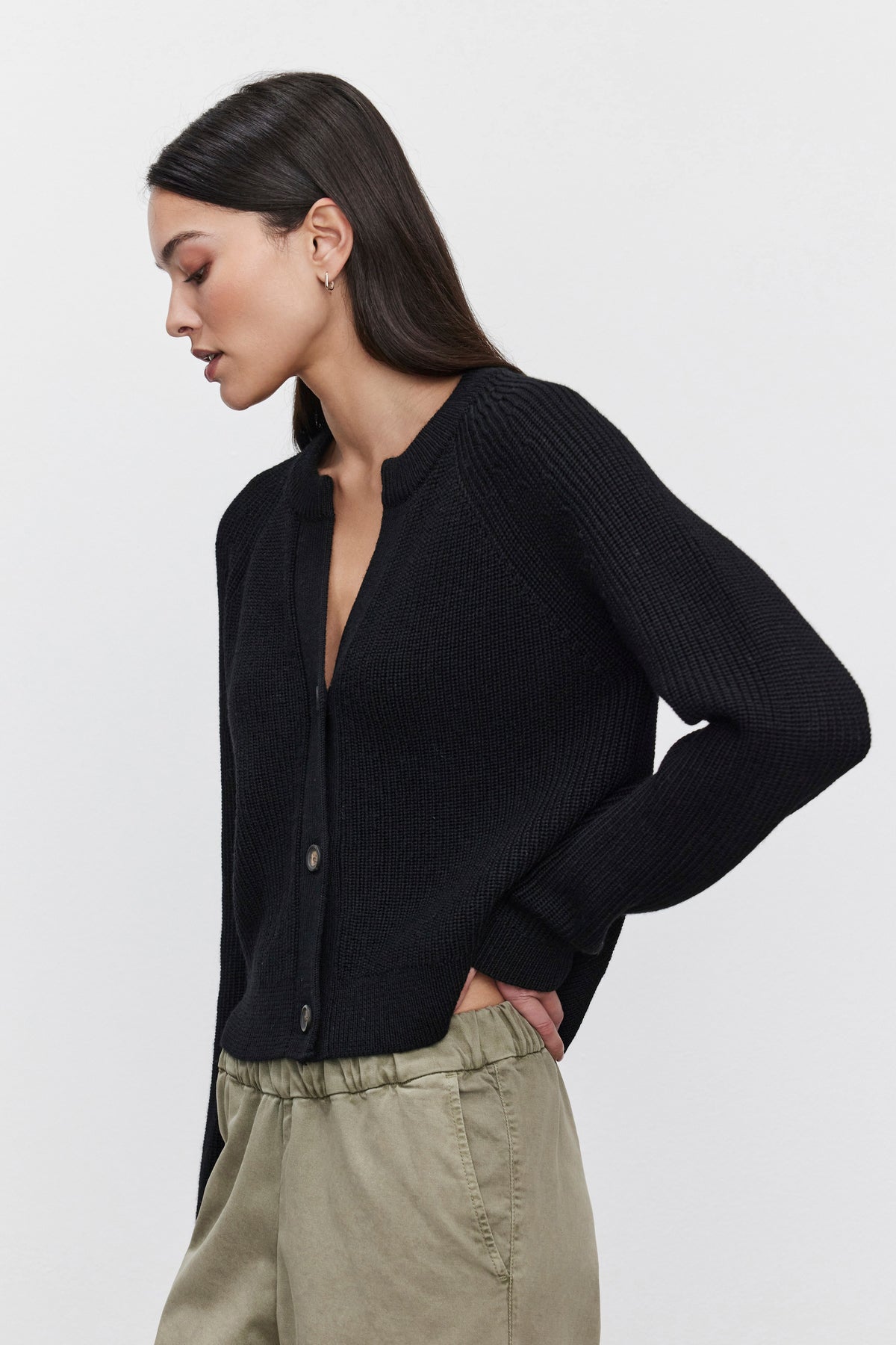   A woman modeling the SHAYLA CARDIGAN from Velvet by Graham & Spencer, a cozy black button-up, paired with khaki pants and her hands in her pockets, posed against a plain white background. 