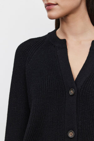 Close-up of a person wearing the SHAYLA CARDIGAN, a cozy black buttoned piece with a textured knit pattern from Velvet by Graham & Spencer. Crafted from a wool blend, the focus is on the garment, highlighting its rich fabric alongside part of the person's face.