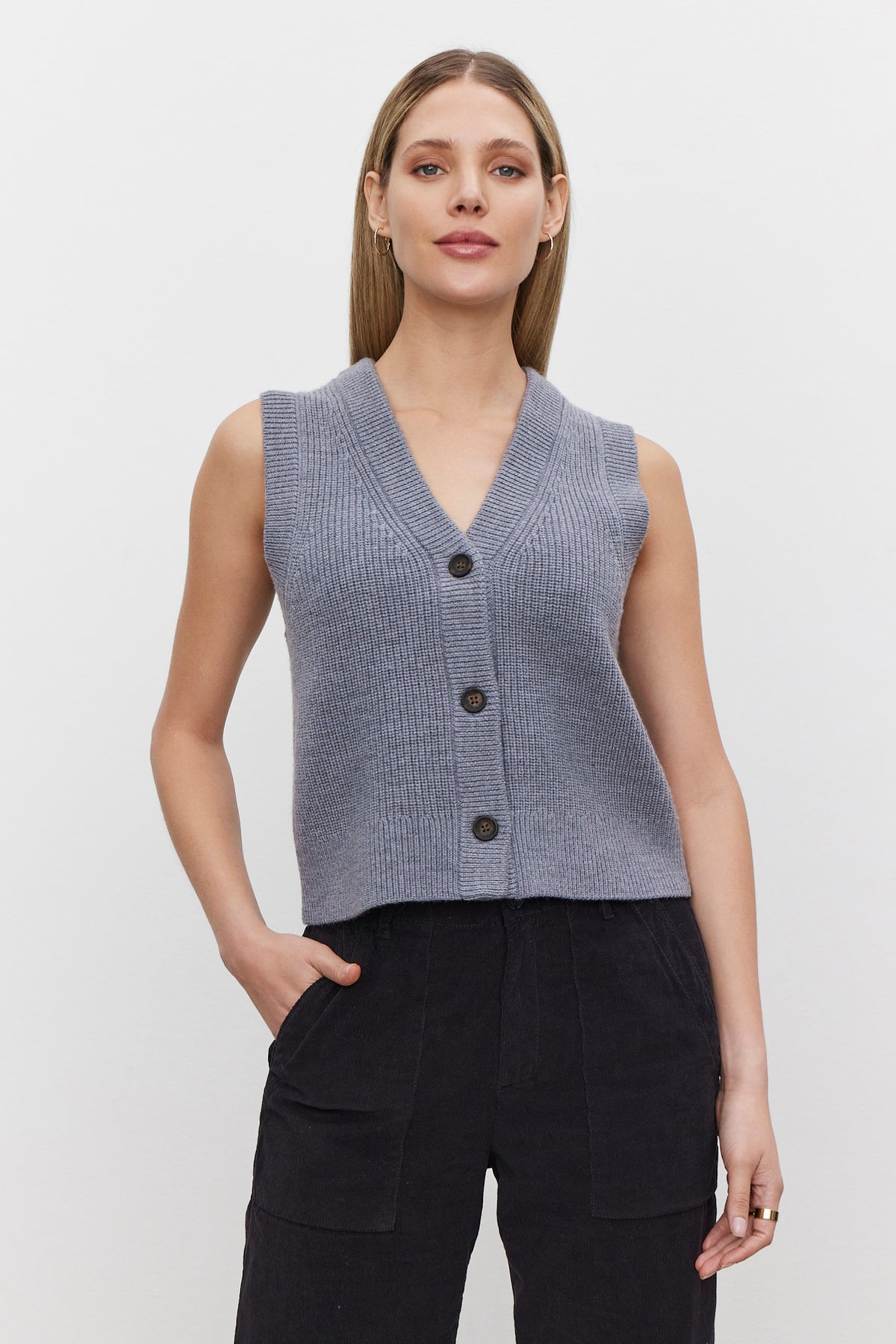 A person wearing the LU SWEATER VEST, a sleeveless gray knit top with a v-neckline from Velvet by Graham & Spencer, paired with black pants, stands against a plain white background.-37665570619585