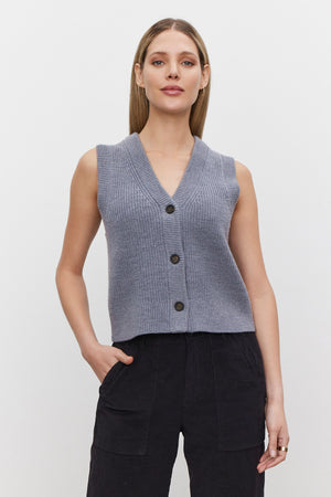 A person wearing the LU SWEATER VEST, a sleeveless gray knit top with a v-neckline from Velvet by Graham & Spencer, paired with black pants, stands against a plain white background.