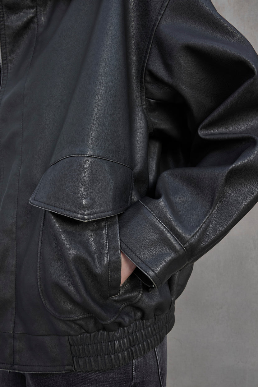 Close-up of a person wearing the CALIFORNIA FAUX LEATHER JACKET by Velvet by Jenny Graham, featuring a loose fit with their hand in a pocket. The black jacket boasts a side flap pocket and elastic cuffs.