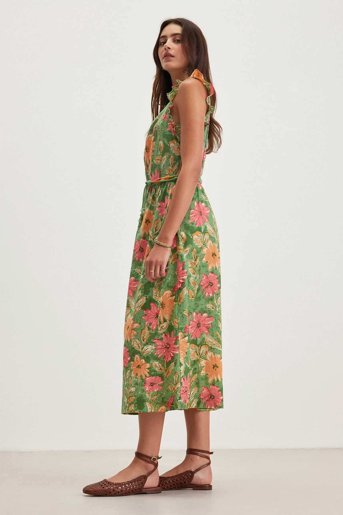 A person in the ELARIA DRESS by Velvet by Graham & Spencer, featuring a lightweight floral print and flutter sleeves, stands sideways, looking forward while wearing brown woven shoes and a simple bracelet.-38662636798145