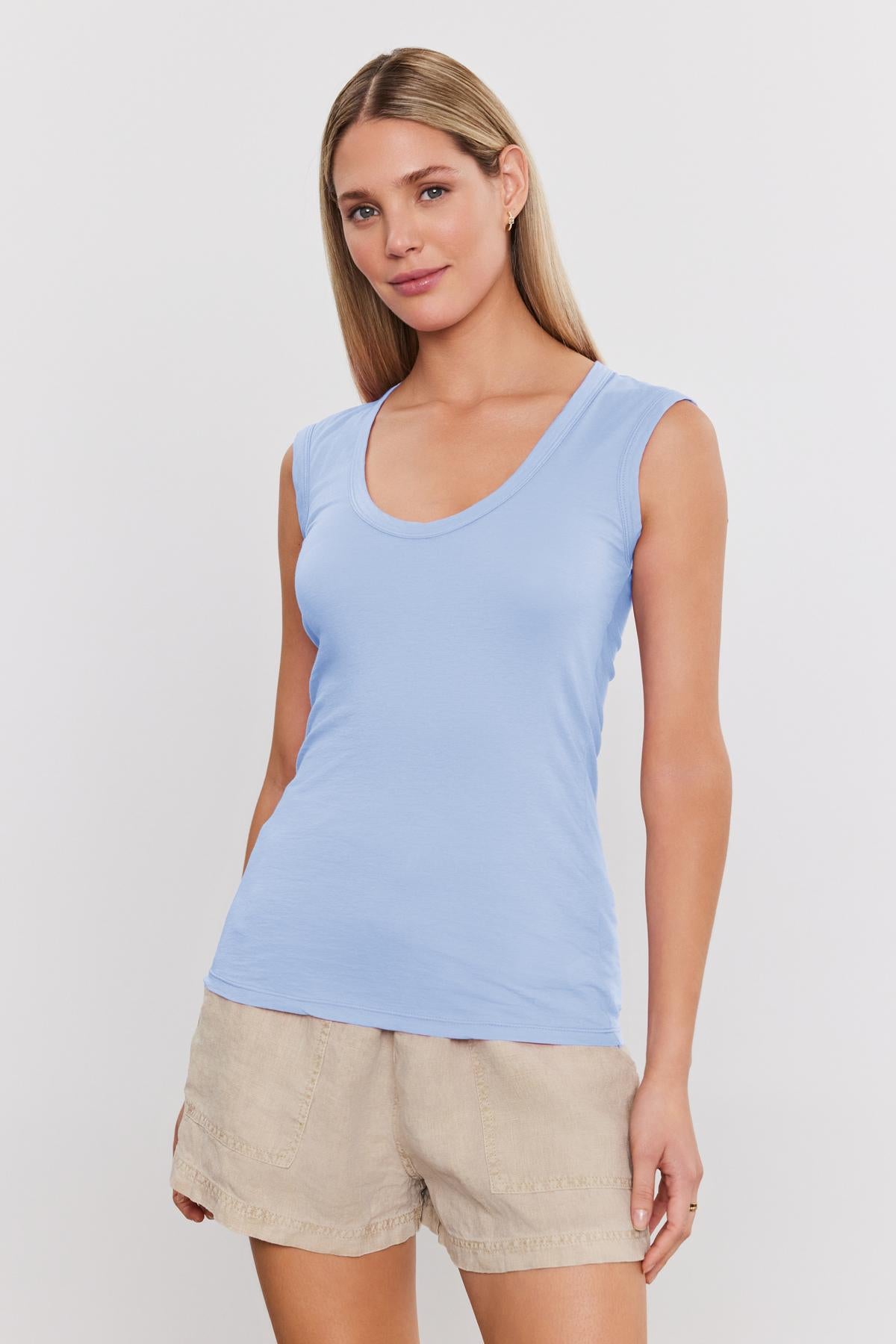   Woman in an ESTINA TANK TOP by Velvet by Graham & Spencer and beige shorts stands against a plain white background, looking at the camera with a neutral expression. 