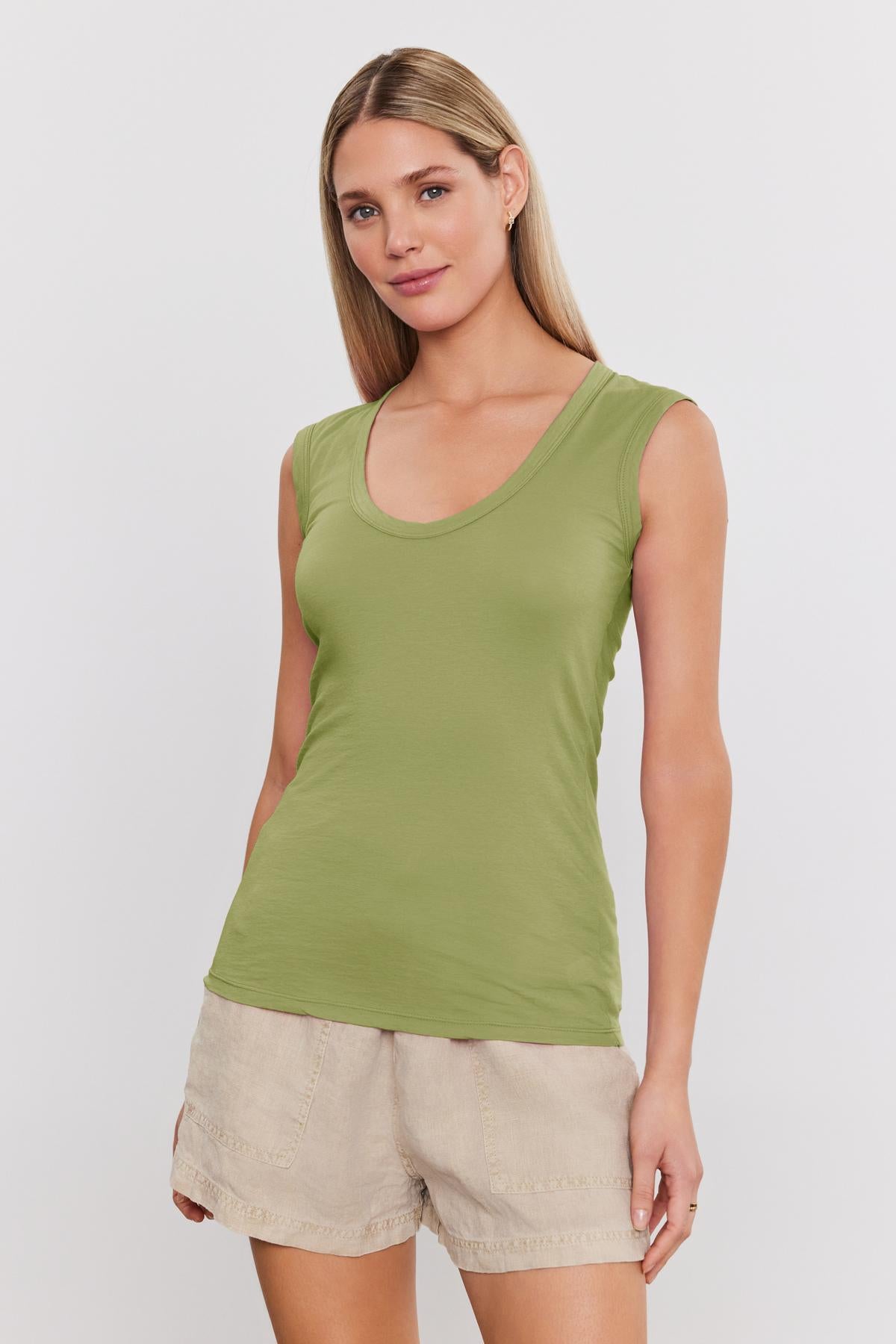   Person with long hair wearing a green ESTINA TANK TOP by Velvet by Graham & Spencer and beige shorts, standing against a white background. 